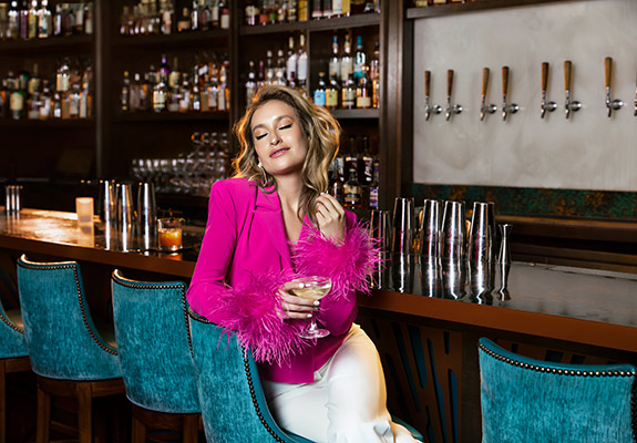 Woman in pink jacket sitting in a blue bar chair. Concept by Gold Dog Communications.